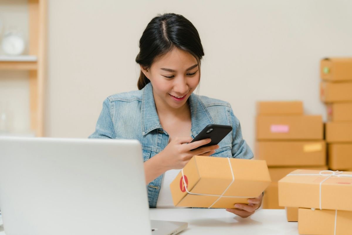 A person at a bright desk checking a parcel against an order on a laptop